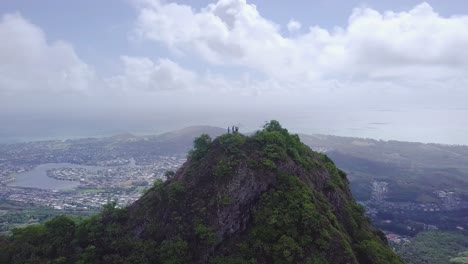 people-standing-on-top-of-a-tall-grassy-mountain-in-Oahu-Hawaii-Honolulu,-AERIAL-ORBIT