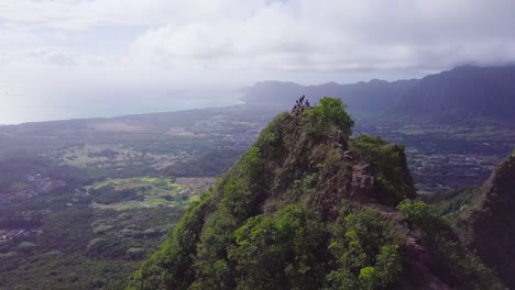 Green-jagged-mountain-in-Honolulu-Hawaii-Oahu-with-hikers-that-finished-their-journey-ascending-it-relaxing-at-the-top,-AERIAL-DOLLY-PULLBACK