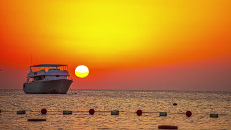 Luxury-Boat-anchored-on-Ocean-water-in-front-of-orange-sunset-time-in-background---time-lapse
