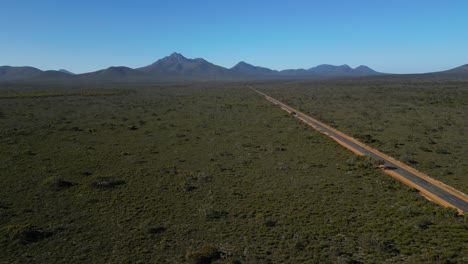 Tracking-aerial-shot-of-empty-road-in-Australian-outback,-mountain-ranges-in-distance
