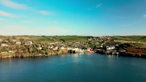 Wide-aerial-panorama-over-calm-blue-waters-towards-an-Irish-village-with-green-hills-on-a-sunny-day-in-January