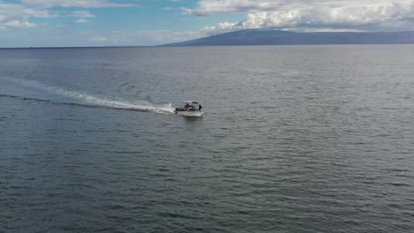 Flat-bottom-boat-cruising-on-open-ocean,-aerial-wide-tracking-Molokai