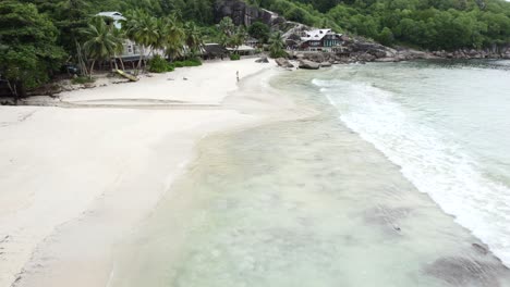 Mahe-seychelles-cinematic-drone-footage-along-Takamaka-beach,-people-on-the-beach-and-eating-in-restaurant