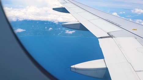 Landscape-of-Timor-Leste-coastline,-beautiful-blue-ocean,-and-view-of-wing-from-commercial-airplane-airplane-window-flying-into-capital-Dili,-East-Timor-in-Southeast-Asia