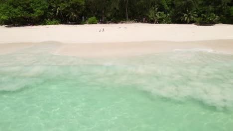 Mahe-Seychelles-Intendance-Beach,-Hombre-Corriendo-Y-Buceando-En-La-Ola-Del-Océano,-Clientes-Sentados-En-La-Playa,-Día-Cálido-Y-Soleado