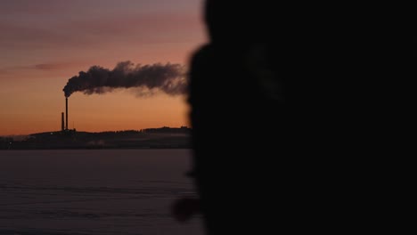 Person-walks-in-front-of-the-camera,-silhouette-of-smoking-power-plant-on-the-background