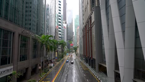 Raining-day-scene-of-the-street-with-moving-traffic,-highrise-skyscraper-office-financial-building-tower-in-the-Central-Business-District,-Robinson-Road,-Singapore