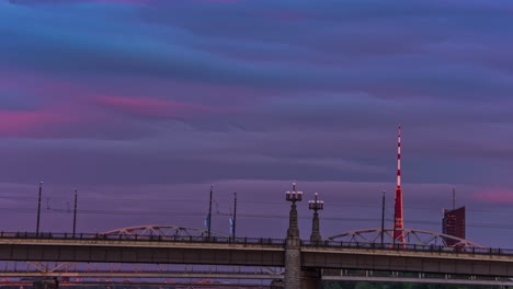 Riga-Tv-Tower-Bridge-Für-Autos-über-Den-Fluss-Daugava-Mit-Farbenfrohem-Sonnenuntergangshimmel,-Fusionszeitraffer