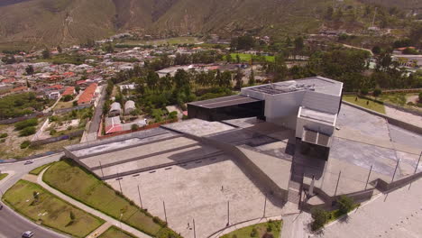 Drone-Volando-Alrededor-De-Un-Gran-Edificio-Moderno-Con-La-Ciudad-De-Quito-En-El-Fondo