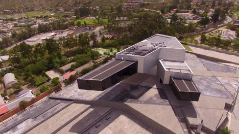 Drone-displaying-a-large-modern-building-with-a-Ecuadorian-mountain-city-in-the-distance