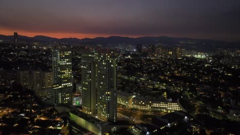 Aerial-view-away-from-the-Arcos-Bosques-shopping-complex,-dusk-in-Mexico-city---pull-back,-drone-shot