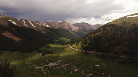 Aerial-View-of-a-scenic,-moody,-and-green-mountain-valley-range-with-winding-road-in-the-Rocky-Mountain-area-of-Colorado