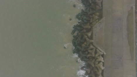 Aerial-establishing-view-of-Port-of-Liepaja-concrete-pier,-Baltic-sea-coastline-,-foggy-day-with-dense-mist,-moody-feeling,-big-storm-waves-splashing,-descending-birdseye-drone-shot