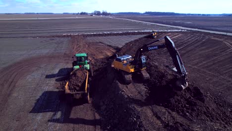 Excavator-grabs-soil-and-moves-it-on-tractor-in-rural-landscape