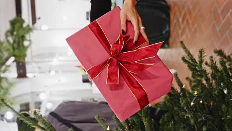 Hand-of-woman-wearing-ring-put-gift-under-Christmas-tree,-vertical-video