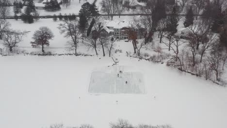 Aerial,-family-and-friends-ice-skating-in-backyard-pond-ice-rink