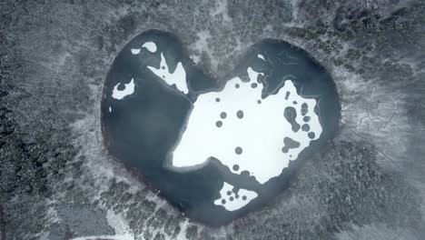 A-static-aerial-shot-over-heart-shaped-frozen-lake-surrounded-by-a-snow-covered-forest
