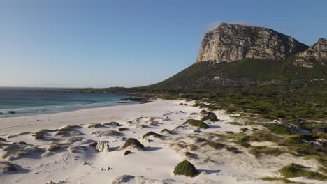 White-sandy-bay-on-a-clear-sky-day-with-a-large-cliff-in-the-background-Moonlight-Beach,-Pringle-bay