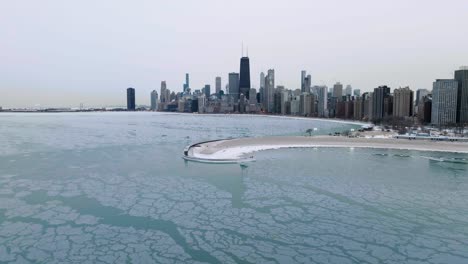 Aerial-view-over-icy-lake-Michigan,-approaching-the-North-Avenue-beach-and-the-skyline-of-wintry-Chicago,-USA