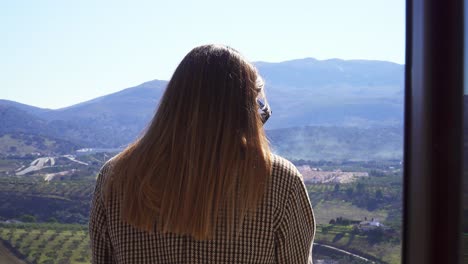 Caucasian-girl-with-straight-hair-and-a-checkered-coat-with-her-back-to-the-camera-on-a-sunny-background-of-mountains-and-fields
