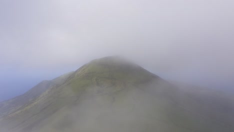 Drone-dolly,-low-clouds-revealing-vulcanic-mountain,-Pico-da-Esperança,-covered-in-lush-green-in-São-Jorge-island,-the-Azores,-Portugal