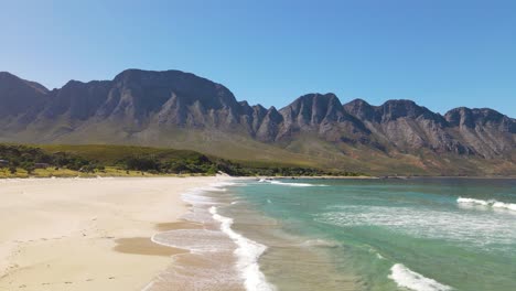 White-sand-beach-with-clear-blue-ocean-with-beautiful-mountains-in-the-background,-Kogel,-South-Africa