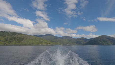 White-water-from-boat-contrasts-with-lush-green-landscape-and-clouds-in-summertime---Endeavour-Inlet,-Marlborough-Sounds