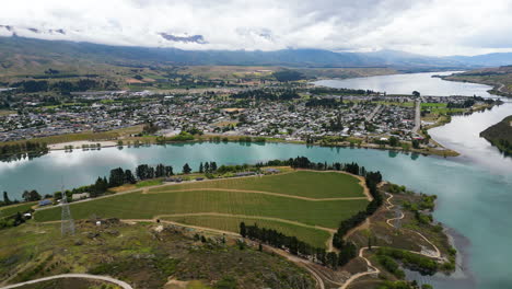 Aerial-circling-Cromwell-town-and-Dunstan-lake-on-cloudy-day,-New-Zealand