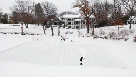 Person-shoveling-snow-alone-to-make-outdoor-ice-hockey-skating-rink,-aerial