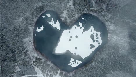 Blick-Von-Oben-Nach-Unten-Auf-Den-Zugefrorenen-See,-Der-In-Einem-Schneebedeckten-Wald-Herzförmig-Ist