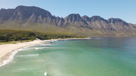 Dynamic-aerial-shot-of-green-can-calm-sea-and-big-mountain-formation-in-the-background-near-Cape-Town