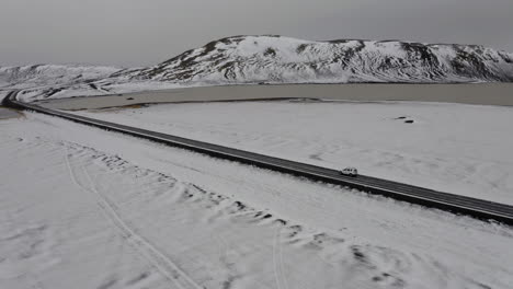 Aerial:-Side-follow-of-car-driving-on-a-snowy-road-in-Iceland