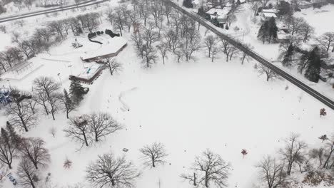 Aerial,-community-suburb-park-covered-in-snow-during-winter,-leafless-treees