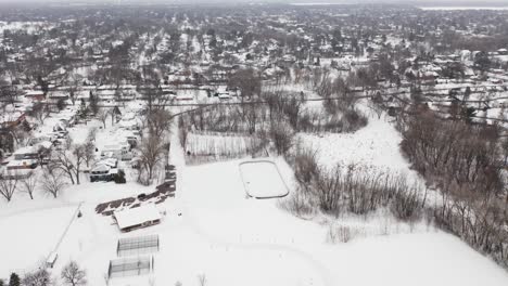 Aerial,-community-skating-rink-in-a-snow-covered-suburb-neighborhood-during-winter