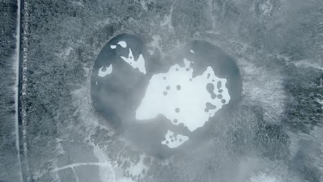Heart-shaped-frozen-lake-in-snowy-forest-from-top-down-view-cinematic-aerial-descending-shot