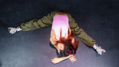 Attractive-young-woman-with-sportswear-stretching-in-splits-on-the-floor-in-a-dance-studio,-top-view