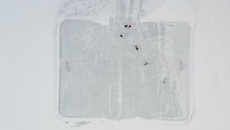 Aerial-top-down,-people-playing-ice-hockey-on-small-outdoor-rink-on-frozen-lake