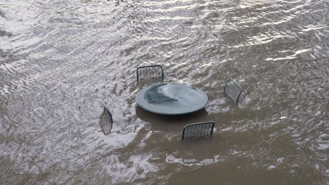 Schwere-Überschwemmung-Vom-Fluss,-Der-Tisch-Und-Stühle-Im-Freien-Eintaucht---Aus-Einem-Anderen-Winkel