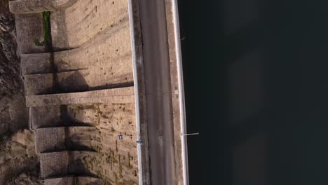Top-down-aerial-view-of-Dam,-drone-flying-above-road,-between-water-and-wall