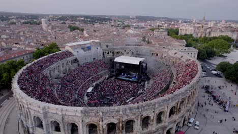 Drone-advance-over-the-Arena-of-Nîmes-at-sunset,-people-are-waiting-for-the-stromae-concert