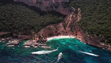 Aerial-view-of-tour-boat-cruise-on-turquoise-sea-in-mountain-coast-bay