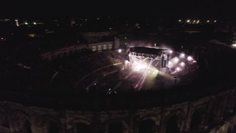 Drone-to-lend-on-the-Arenas-de-Nîmes-in-the-middle-of-the-night,-people-are-watching-the-concert-and-there-are-lights-of-several-colors