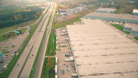 Buildings-of-logistics-center,-warehouses-near-the-highway,-view-from-height,-a-large-number-of-trucks-in-the-parking-lot-near-warehouse