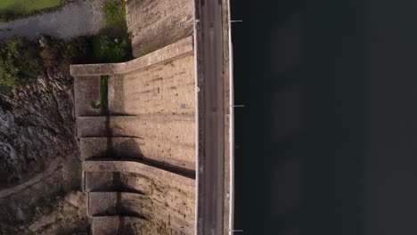 Top-down-aerial-of-Dam,-drone-rises-above-road,-golden-hour,-zoom-out