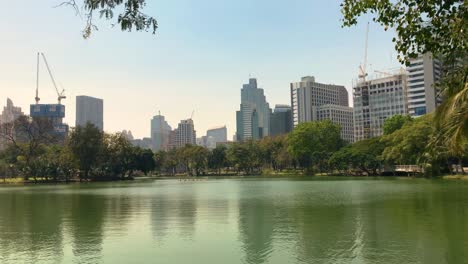 The-landscape-of-Lumphini-Public-Park-with-lake,-panning-view,-and-background-of-the-downtown-building