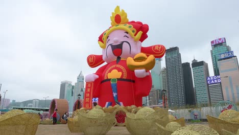 Ein-Mann-Geht-über-Den-Rahmen-Vor-Einer-Installation-Zum-Chinesischen-Neujahrsthema-Für-Das-Chinesische-Neujahrsfest,-Während-Im-Hintergrund-In-Hongkong-Wolkenkratzer-Zu-Sehen-Sind