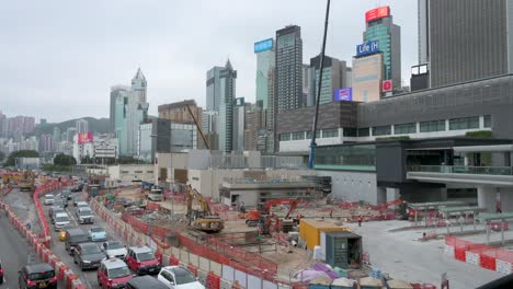 Kräne,-Metallträger-Und-Technische-Ausrüstung-Stehen-Auf-Einer-Baustelle-Als-Teil-Eines-Sanierungsprojekts,-Während-Die-Skyline-Des-Finanzviertels-Von-Hongkong-Im-Hintergrund-Zu-Sehen-Ist