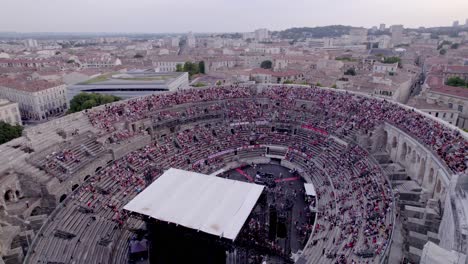 Drone-over-the-Arena-of-Nimes-at-sunset,-people-are-waiting-for-the-stromae-concert