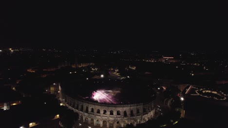 Drone-rotation-on-the-Arenas-de-Nîmes-in-the-middle-of-the-night,-people-are-watching-the-concert-and-there-are-lights-of-several-colors