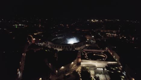 Drone-rotation-on-the-Arenas-de-Nîmes-in-the-middle-of-the-night,-people-are-watching-the-concert-and-there-are-lights-of-several-colors